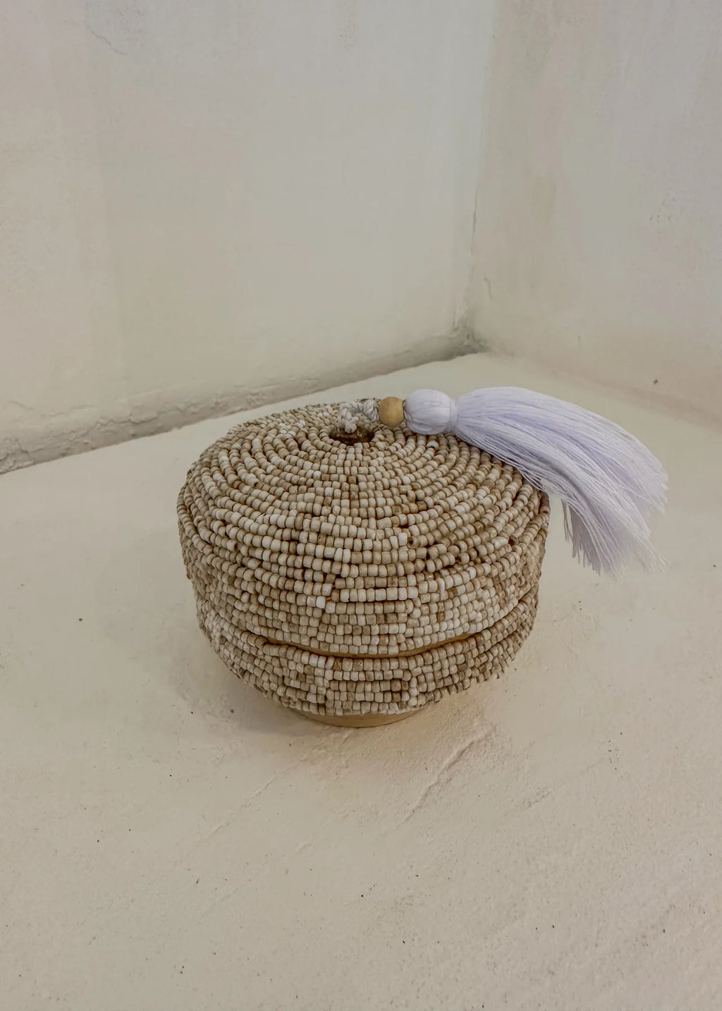 Dit opbergdoosje volledig bedekt met beige glaskralen en afgewerkt met een zachte witte kwast. Perfect om sieraden in op te bergen.