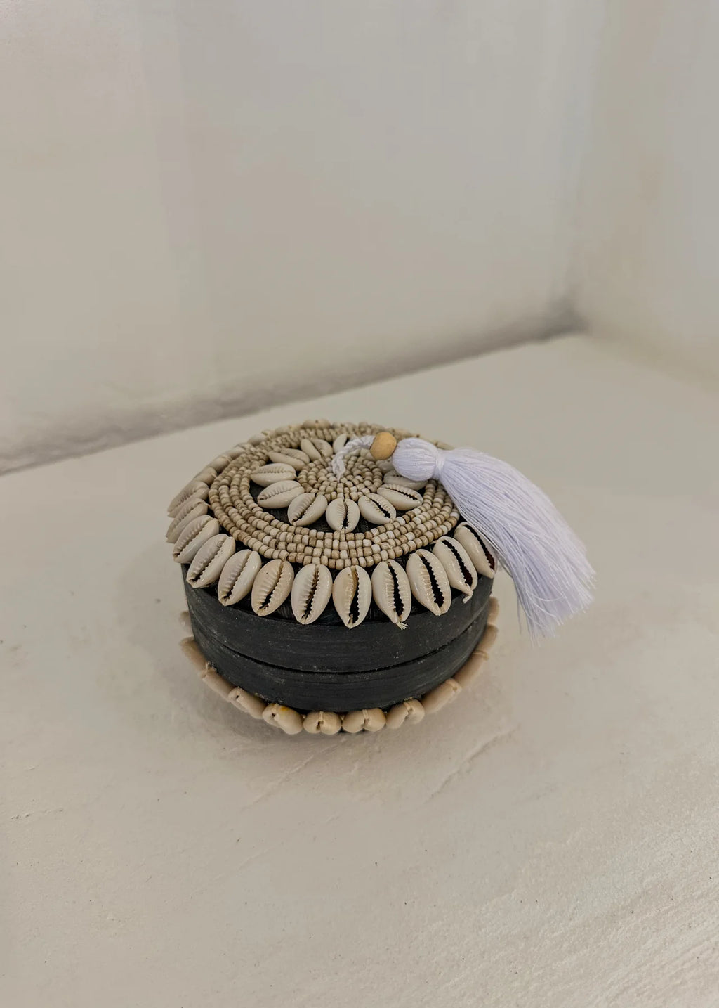 De Nero Shell Box combineert een stoere zwarte basis van bamboe met verfijnde details van kauri schelpen en beige glaskralen.